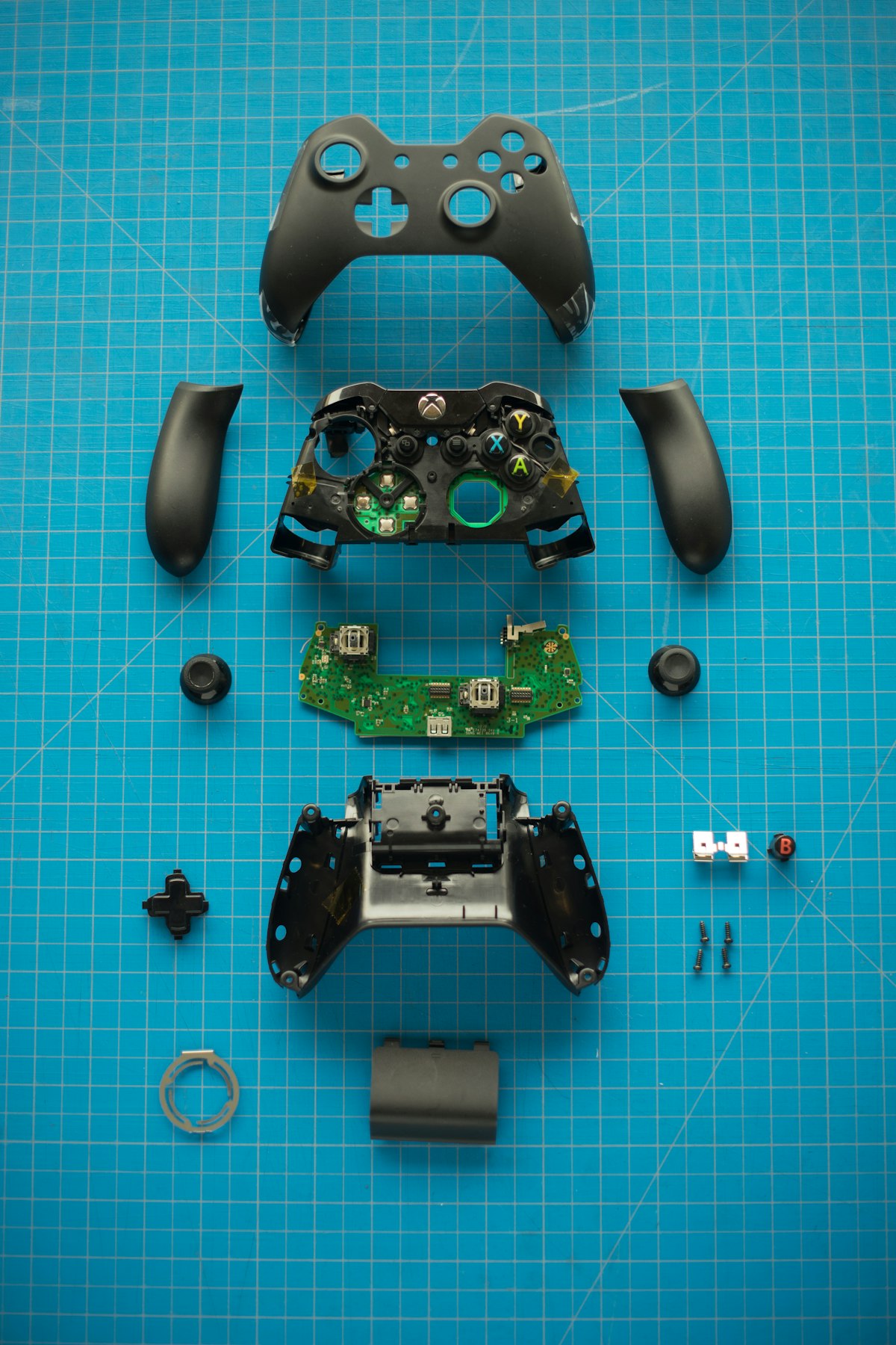 Mando Xbox completamente desmontado con todas sus piezas organizadas sobre una alfombrilla de corte