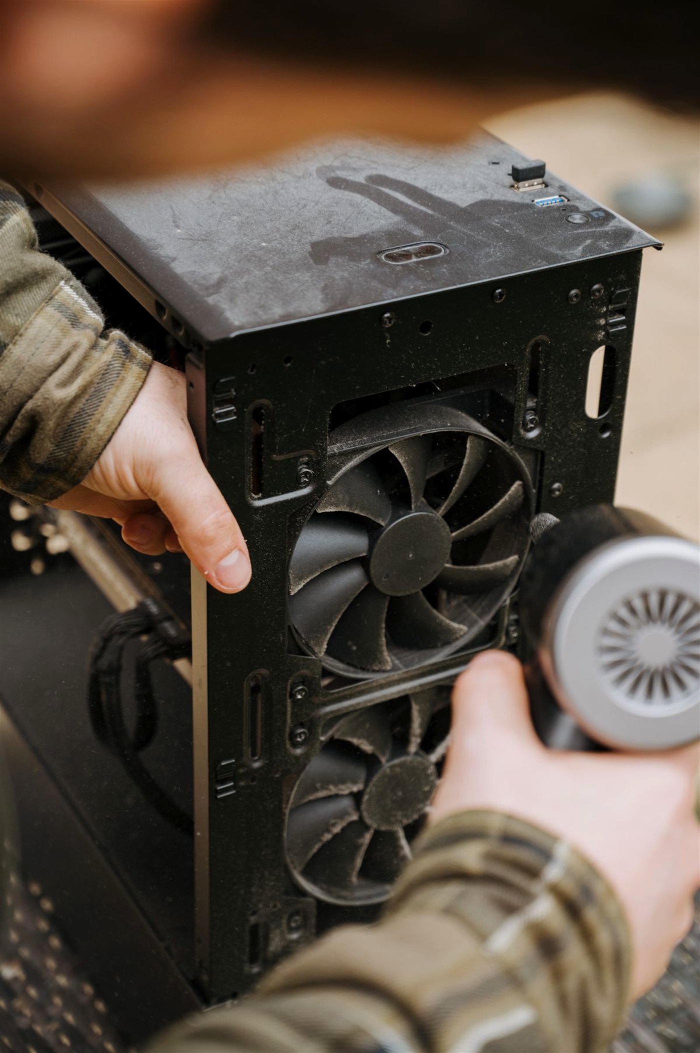 Manos limpiando con aire comprimido el polvo acumulado en los ventiladores del interior de una torre de PC