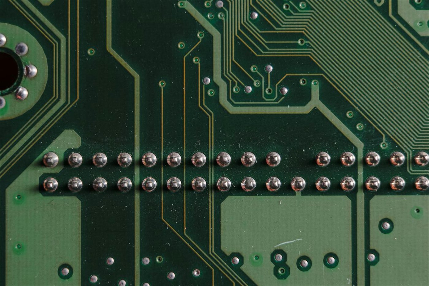 Macro de una fila de juntas de soldadura brillantes y uniformes sobre una placa de circuito verde