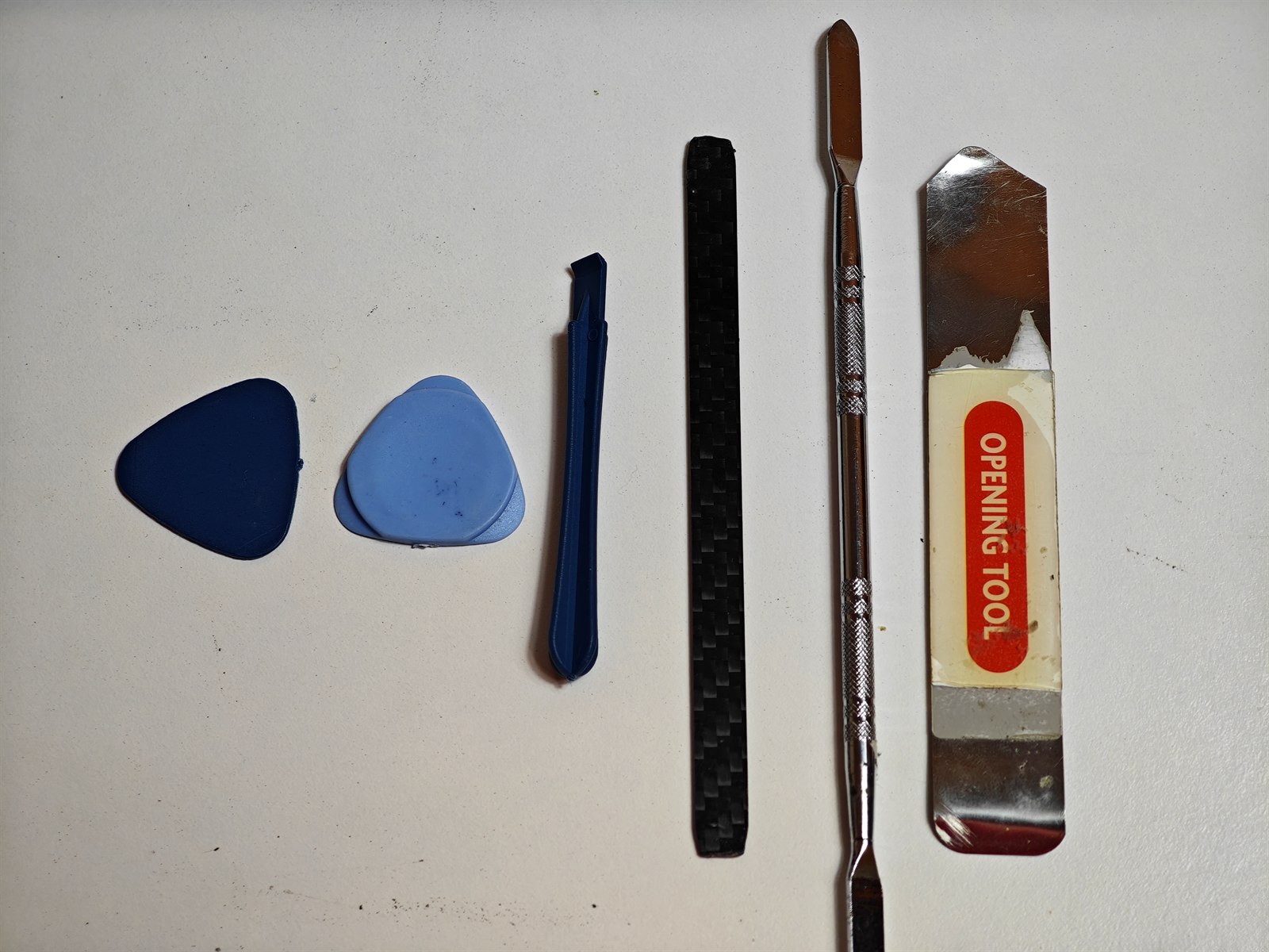 Set de spudgers, púas y palancas de apertura de plástico y nylon junto a una lámina metálica de apertura