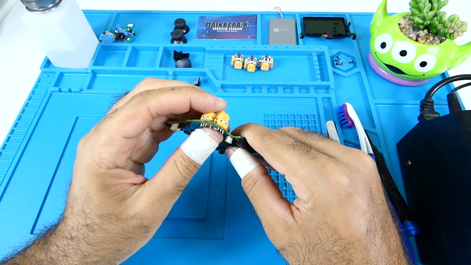 Módulo de joystick de repuesto nuevo sostenido entre los dedos junto a la placa del mando, listo para soldar
