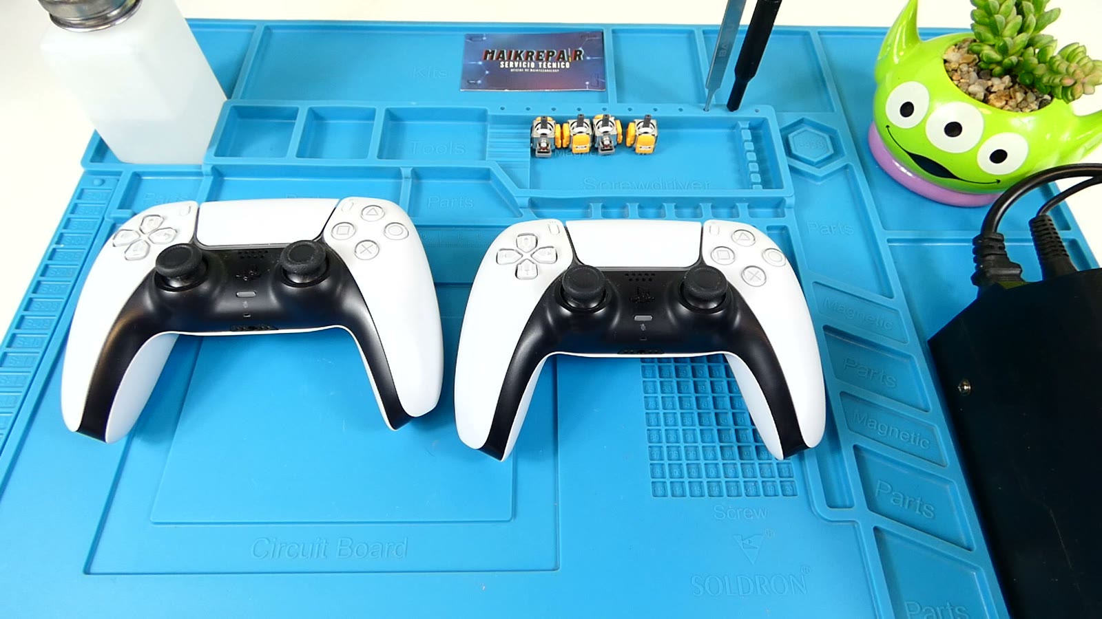 Kit real de reparación: dos mandos DualSense de PS5, cuatro módulos de joystick de repuesto, destornillador de precisión y pinzas sobre una esterilla de trabajo