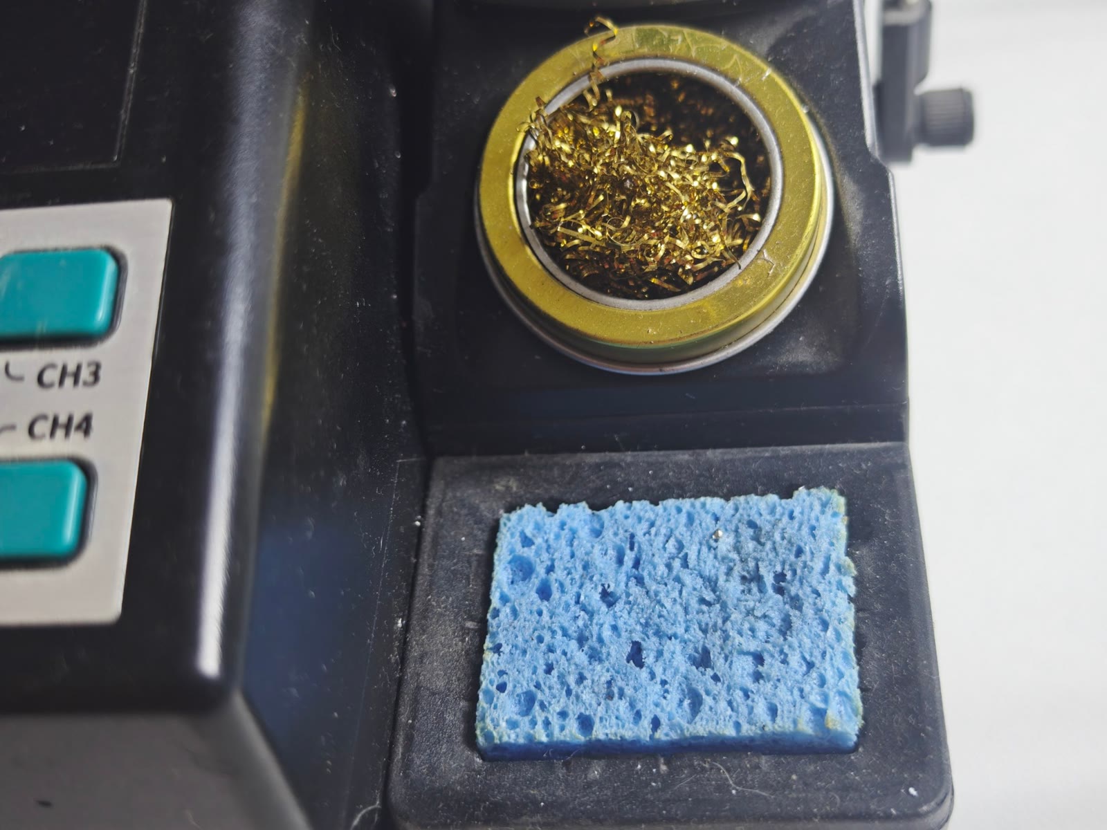 Bola de virutas de latón dorada en su soporte amarillo, junto a una esponja húmeda azul, integradas en la estación de soldadura